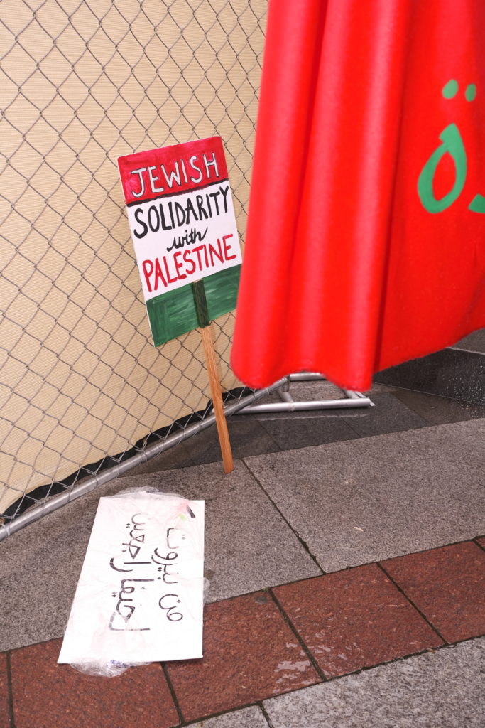 A stray sign against a fence declaring Jewish solidarity with Palestine.