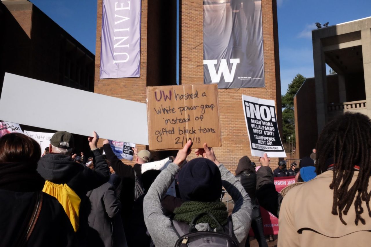 A counter-protester holds a sign that reads "UW hosted a white power group instead of gifted black teens 2/10/18".