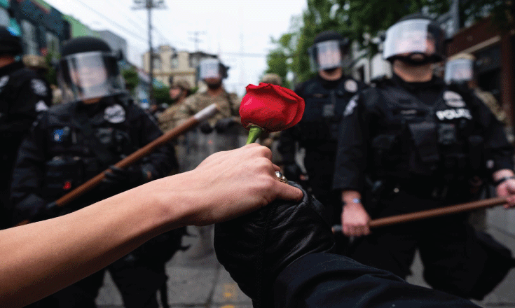 Protestors clasp hands and hold a rose on the front line of a police blockade on Pine Street and 11th Avenue on day 5 of protests.