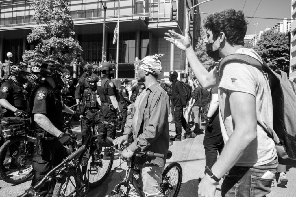 Protestors look onward toward a mass of police officers blocking the next intersection