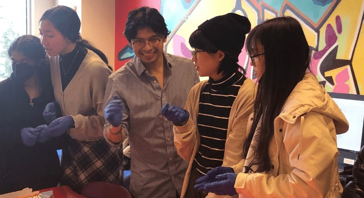 Group of five students with gloves talking at the event.