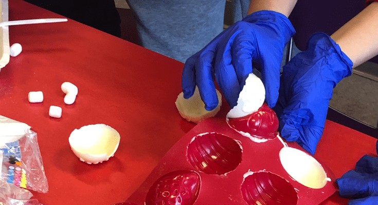 Person wearing blue gloves removing hardened white chocolate from chocolate mold.