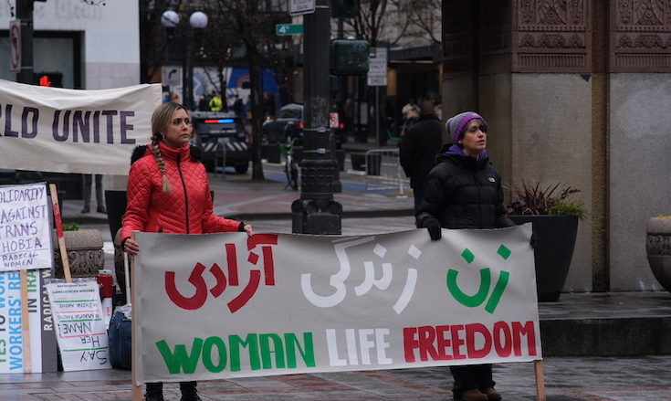 Two group members hold up a “Woman, Life, Freedom” banner in both English and Farsi.